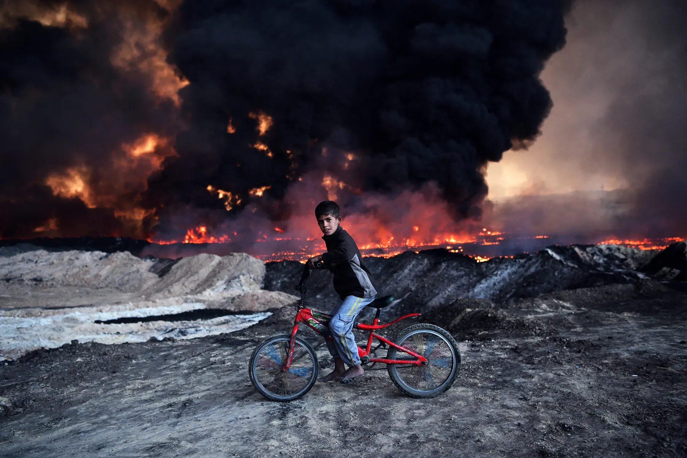 A boy passes  an oil field set  aflame by  retreating ISIS  fighters ahead  of the Mosul  offensive in  Qayyarah, Iraq. CARL COURT/GETTY IMAGES
